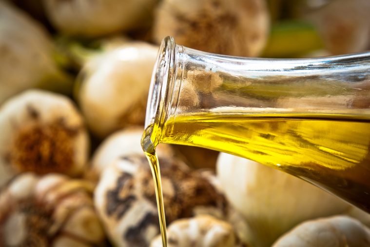 Close-up on pouring extra-virgin olive oil with fresh garlic in the background.