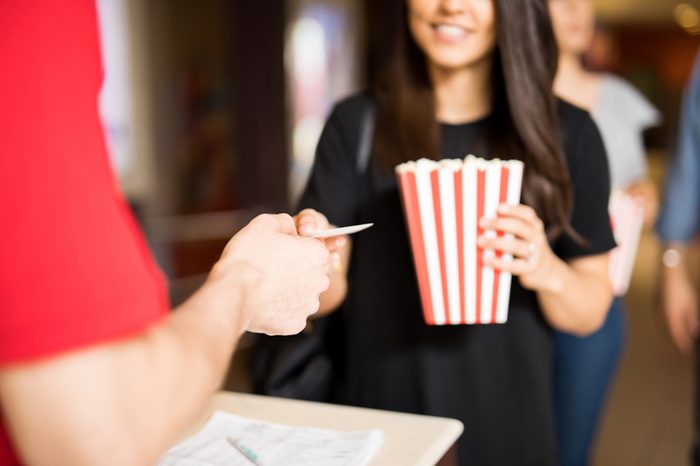 Closeup of a woman holding a bag of popcorn and handing her ticket at the movie theater entrance