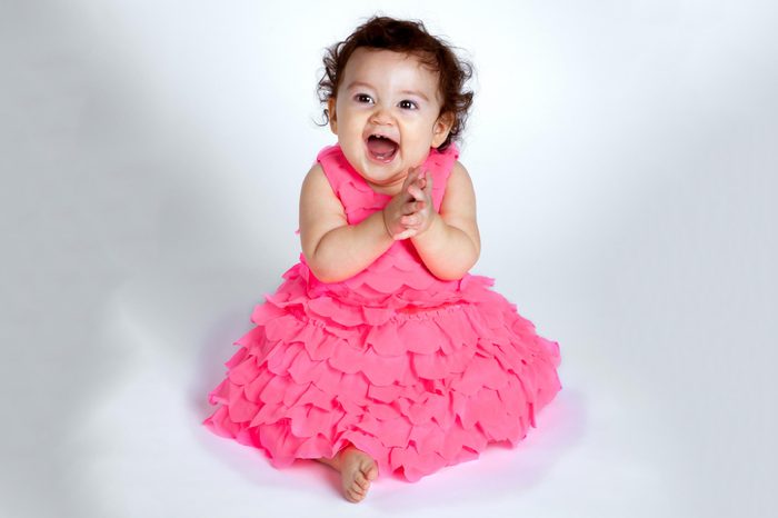 An adorable and happy baby girl sits on a white background clapping her hands and smiling with excitement. She is Native American and Hispanic.