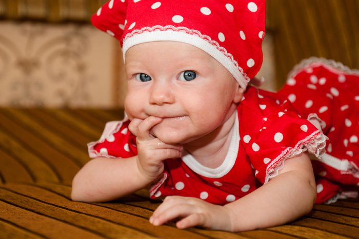 Beautiful expressive adorable happy cute laughing smiling baby infant face. Newborn child relaxing in bed. Nursery for young children. Family morning at home. funny child in a fashionable red dress