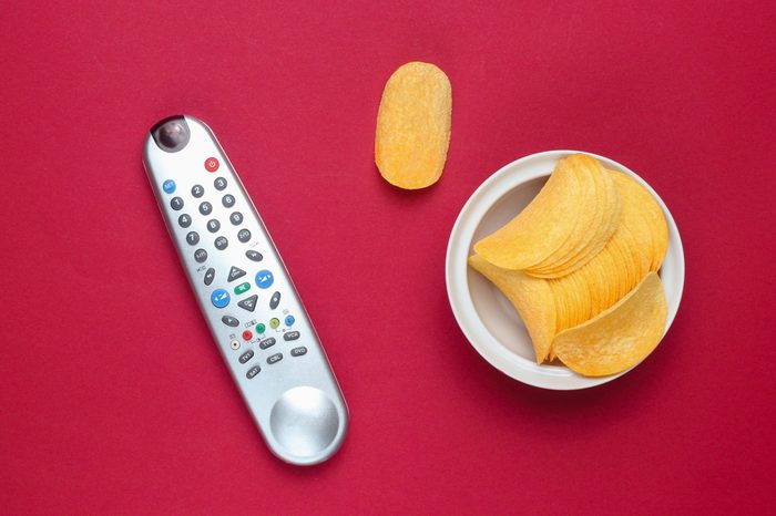 Tv remote, potato chips in a plate on red background. Watching TV, top view