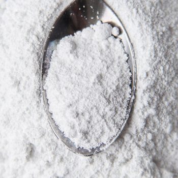 White powder in silver spoon over white background. Top view. Detailed close-up shot. Icing, caster, confectioners or powdere sugar pile.