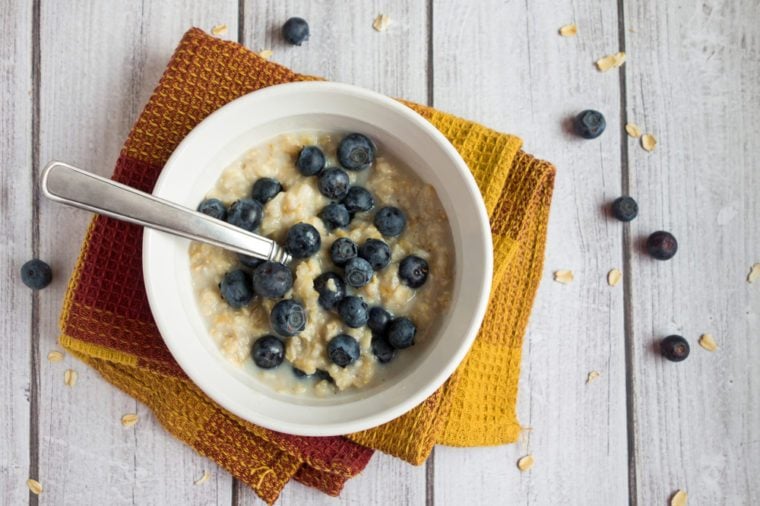 A healthy bowl of hot oatmeal with blueberries with spoon sitting on a light wood surface.