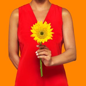 anonymous figure in a red dress holding a single sunflower