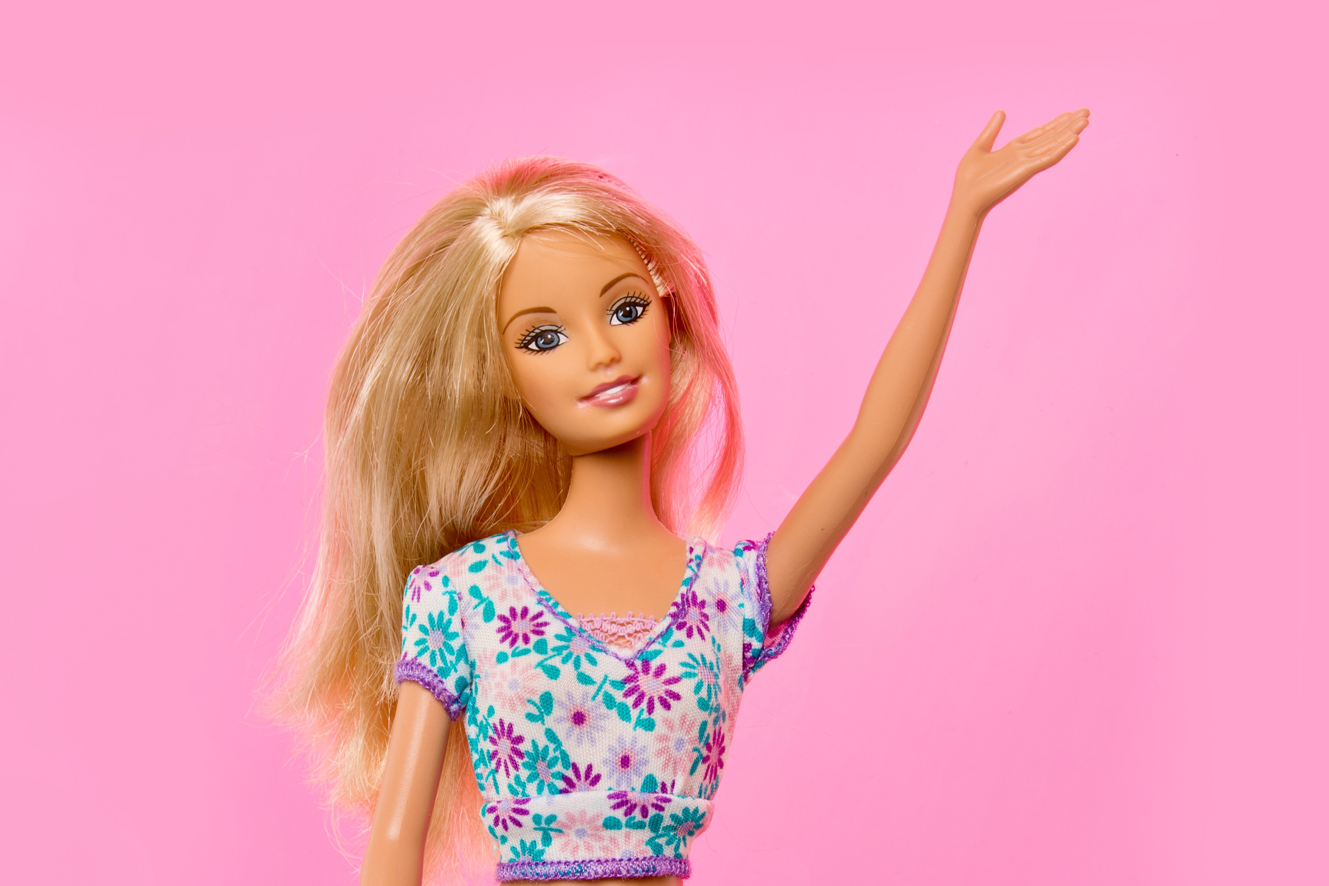 Barbie waving against a light pink background