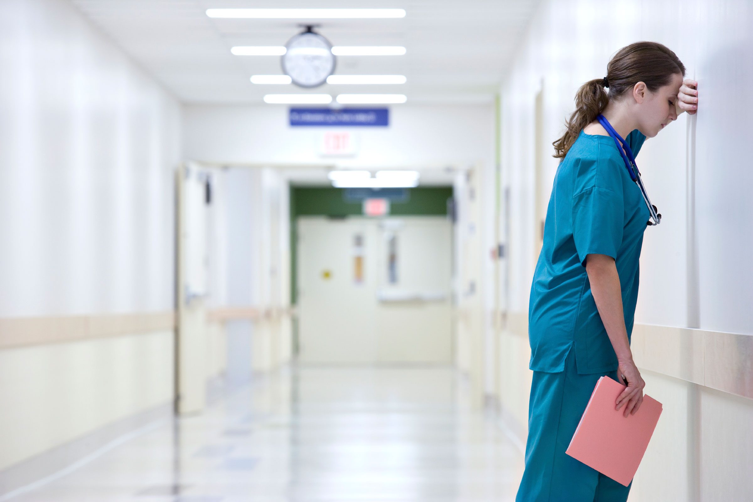 stressed nurse with head against hospital corridor wall