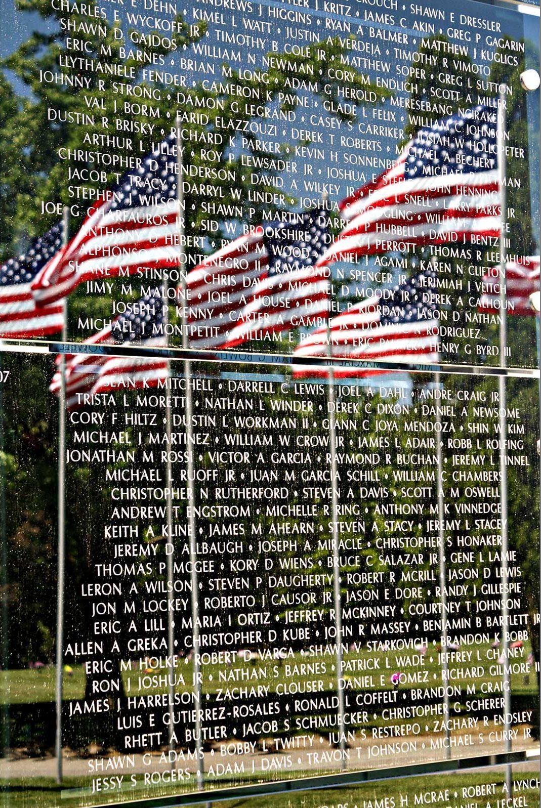 american flags reflected in the glossy surface of a memorial listing the names of those to be remembered