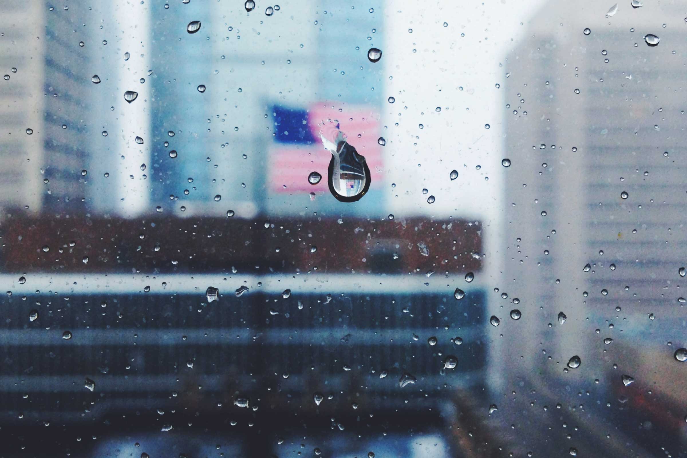 a view of the city of Philadelphia and an american flag through a window with droplets of rain
