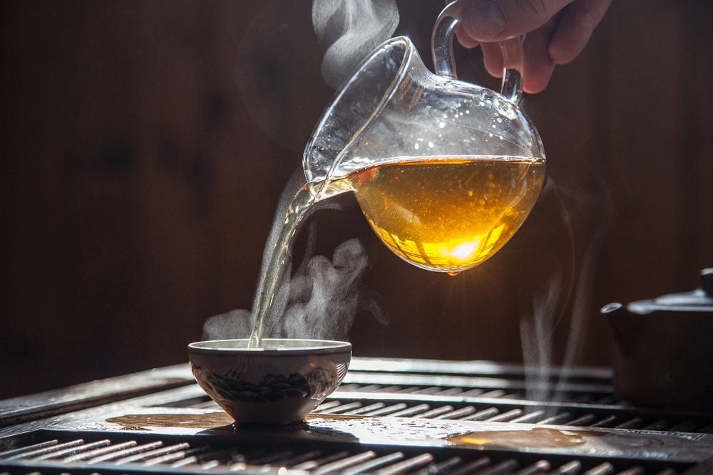 Hand that pours chinese green tea from glass kettle to smal cup