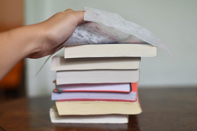 hand using a dryer sheet to clean a stack of old books