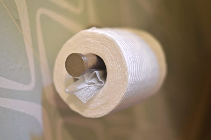 dryer sheet sticking out of a roll of toilet paper mounted on a bathroom wall
