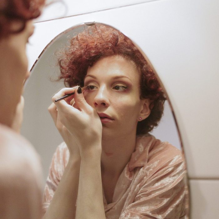 Woman with red hair applying makeup in mirror