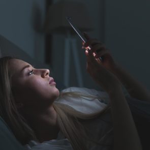 Closeup portrait of young sleepy exhausted woman lying in bed using smartphone, can not sleep/ Insomnia, nomophobia, sleep disorder concept/ Dependency on a cell phone/ Internet addiction