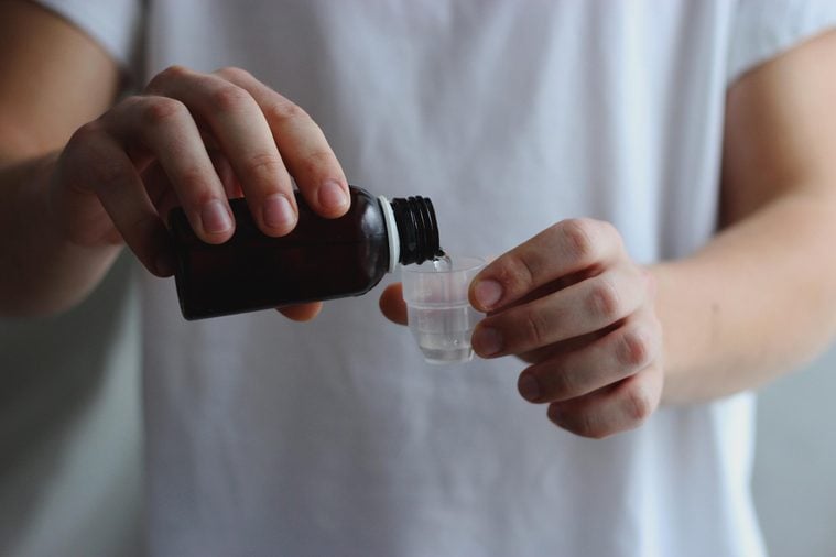 bottle of cough syrup and a beaker in male hands. Pouring cough syrup. The concept of health