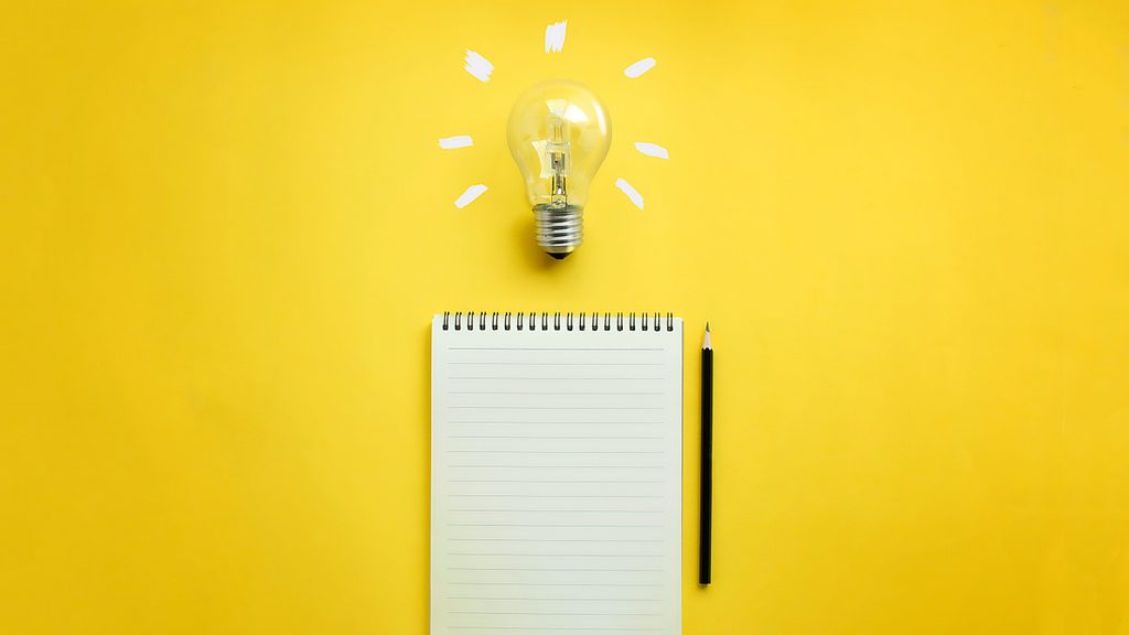 lightbulb, notebook, and pencil on yellow background. writing will make you smarter. note taking concept.