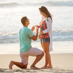man kneeling to propose to his girlfriend on the beach