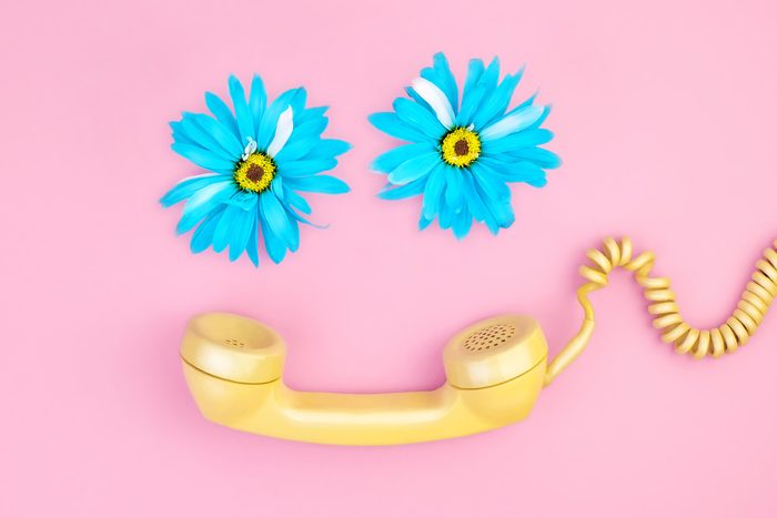 a smiley face made with two blue flowers and a yellow phone with a chord on a pink background