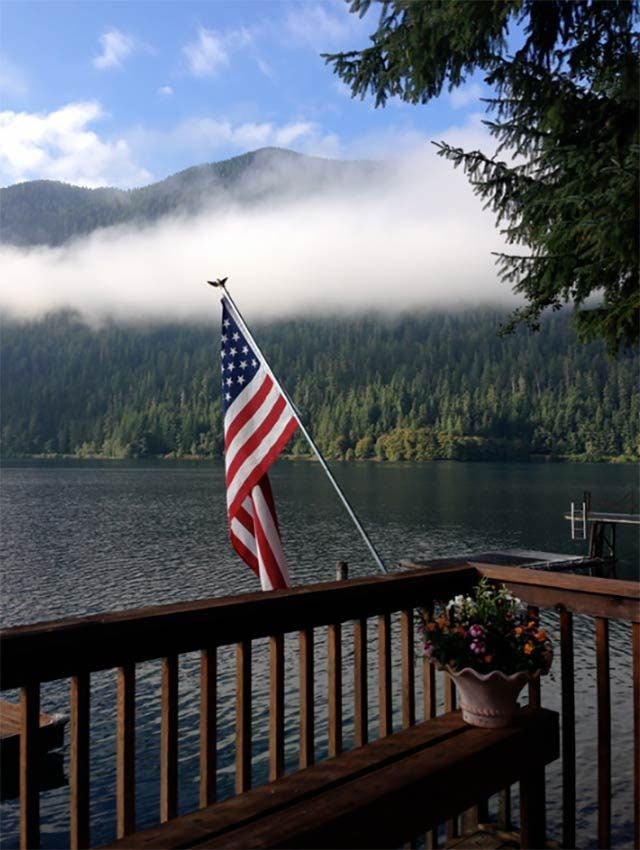 an american flag is proudly displayed on a deck overlooking Lake Crescent with the Olympic Mountains in the background in Washington, USA