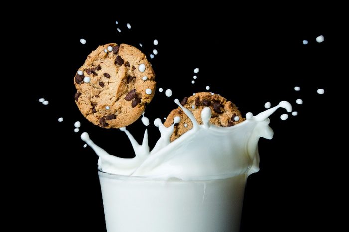 two chocolate chip cookies splashing into a glass of milk. black background.