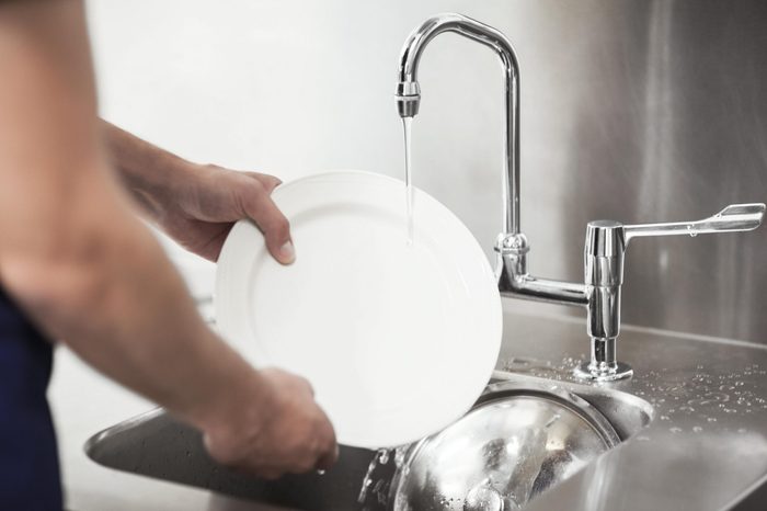 Kitchen porter cleaning white plates in sink in professional kitchen