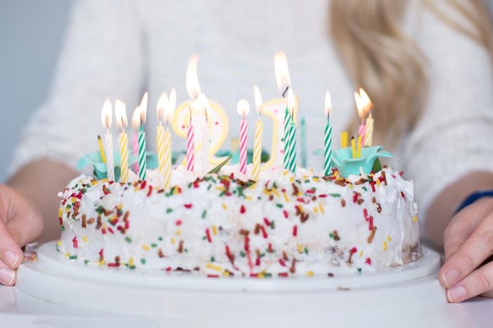 Portrait of a young beautiful blond girl holding plate with birthday cake and blowing candles making a wish