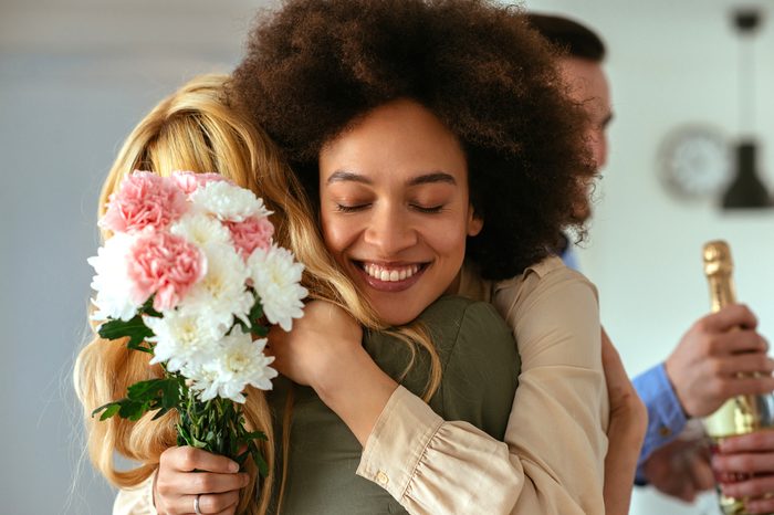 Shot of a woman hugging a friend and holding flowers.