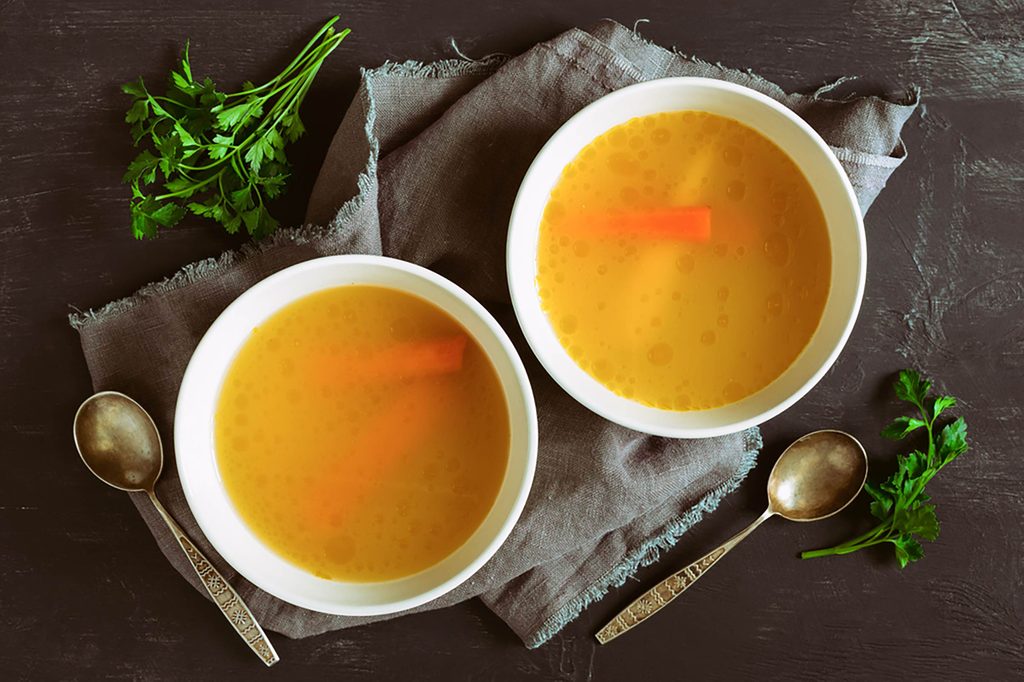 two bowls of broth or stock in white bowls on a wood background