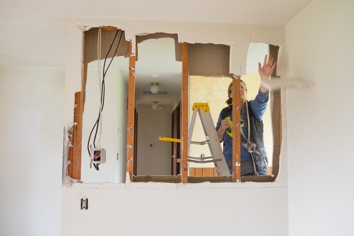 Female construction worker and homeowner using a sawsall tool to cut drywall out and take a wall down to a half-wall during a DIY house renovation.