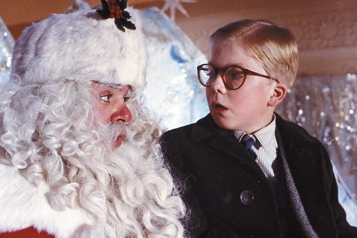 A scene from A Christmas Story of a young boy with glasses is sitting on Santas lap