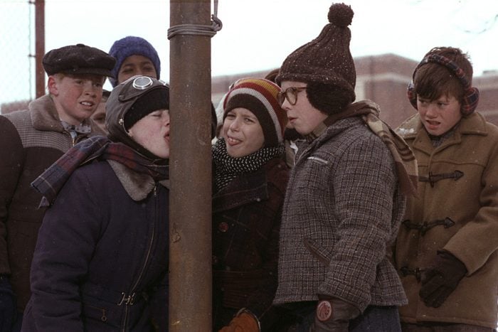 A scene from Christmas Story with a group of school boys in winter clothes and one has his tongue stuck on a street pole
