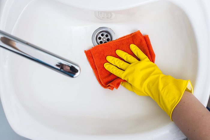 person with cleaning gloves cleaning bathroom sink with cloth
