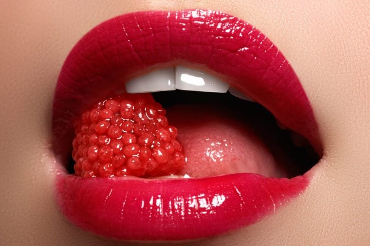Close-up of woman's lips with bright fashion red glossy makeup. Macro bloody lipgloss make-up. Red sexy lips. Open mouth. Manicure and makeup. Make up concept.