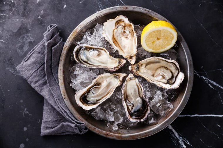 Opened Oysters on metal plate with ice and lemon on dark marble background 