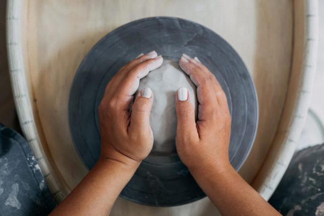Hands of woman potter, ready to work with white clay at pottery wheel, top view, selective focus