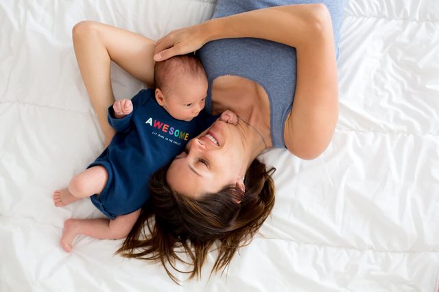 Mother and newborn baby boy, lying in bed, hugging with love, high angle shot, from above. Happy family concept