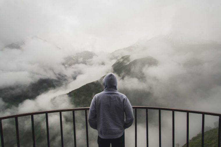 View from behind of a man standing at view point looking to beautiful landscape with foggy mountains in the distance