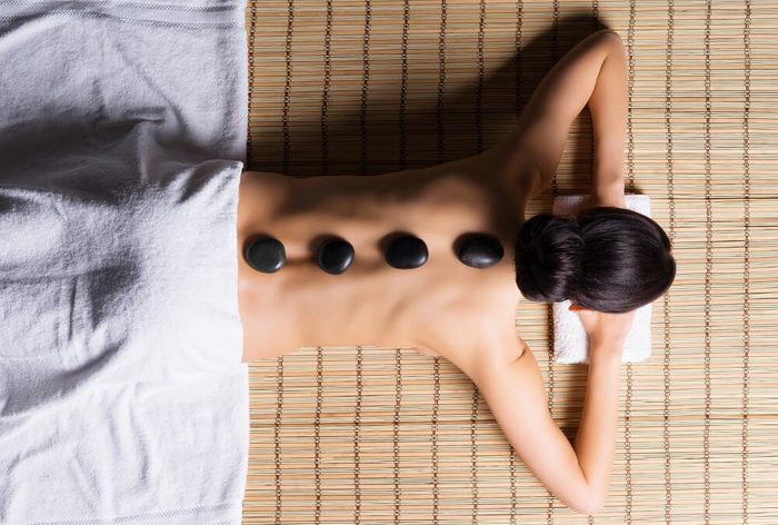 Beautiful, young and healthy woman on bamboo mat in spa salon is having hot stone massage. Spa, health and healing concept. 