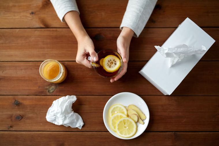 woman drinking tea with lemon, honey and ginger and paper wipes box on wooden table