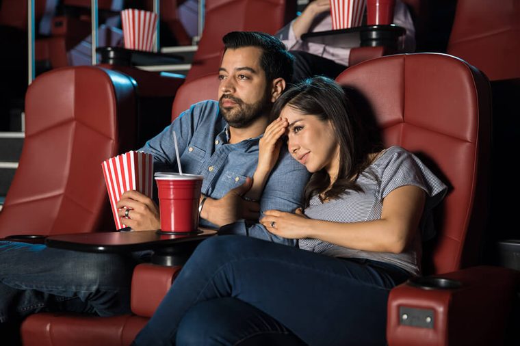 Pretty young woman holding her boyfriend's arm while watching a scary scene in a movie theater