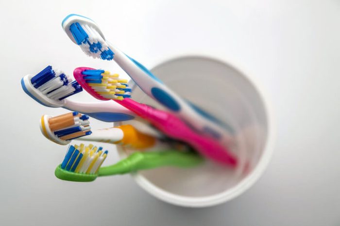Close up shot of set of multicolored toothbrushes in glass on clean toilet on white background, concept dental.