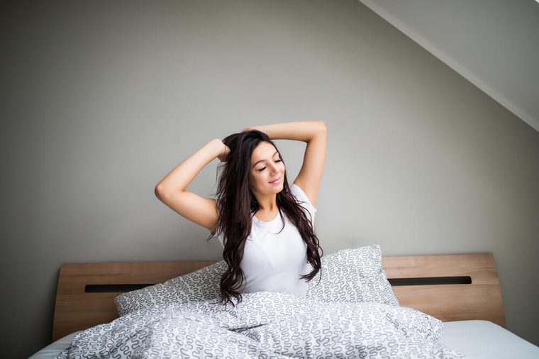 Woman stretching in bed after wake up near big window