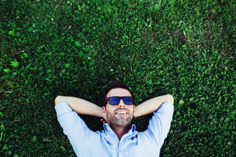 Portrait of a young happy man relaxing on the grass with his hands under the head