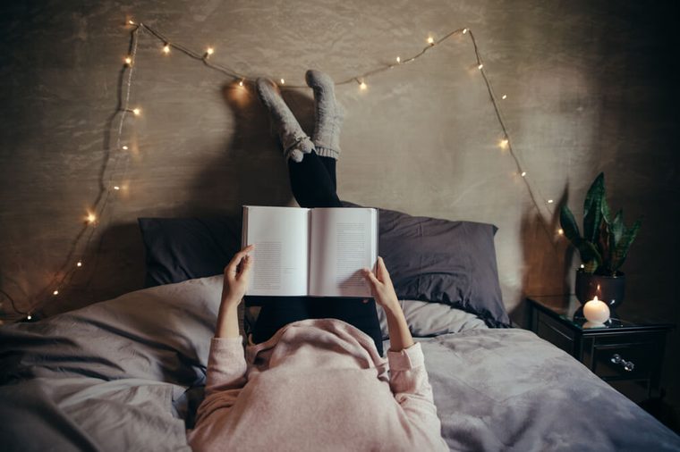 Cropped shot of woman lying on bed and reading book. Female hands holding a book while lying on bed.