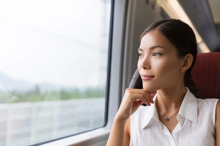 Asian woman traveler contemplating outdoor view from window of train. Young lady on commute travel to work sitting in bus or train.