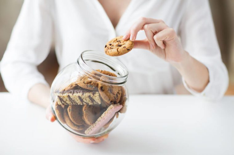 people, junk food, culinary, baking and unhealthy eating concept - close up of hands with chocolate oatmeal cookies and muesli bars in glass jar