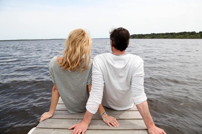 Rear view of couple sitting on a wooden bridge by a lake