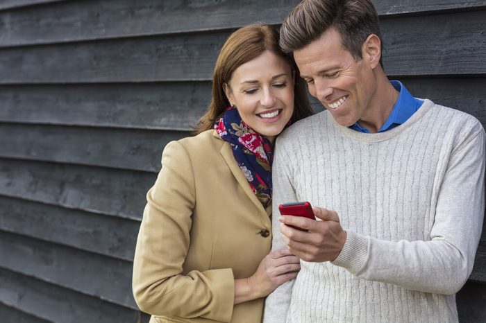Attractive, successful and happy middle aged man and woman couple together outside using mobile cell phone