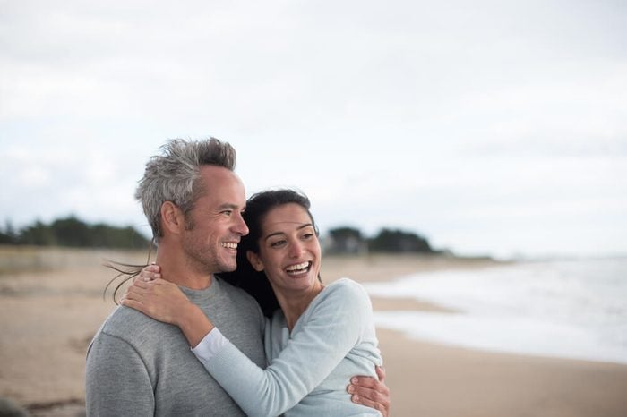 middle-aged couple are walking on the beach, they wear sweaters and jeans
