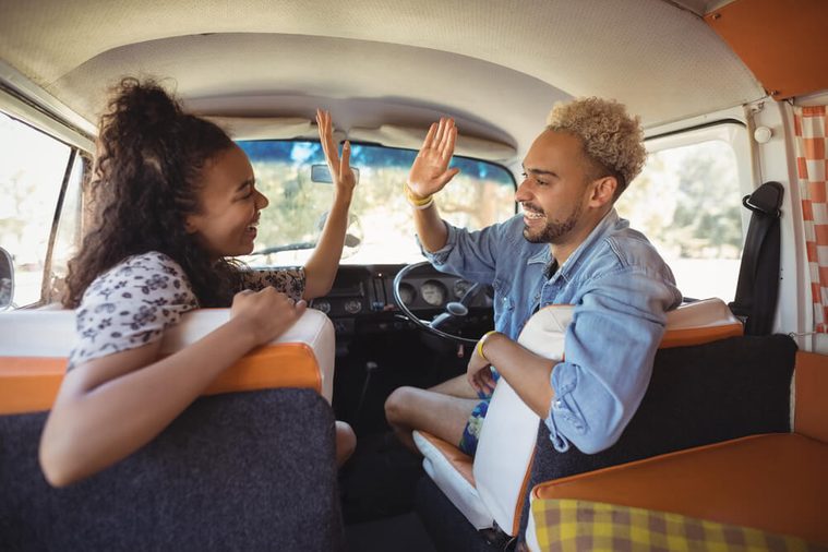 Happy friends giving high-five while sitting in mini van