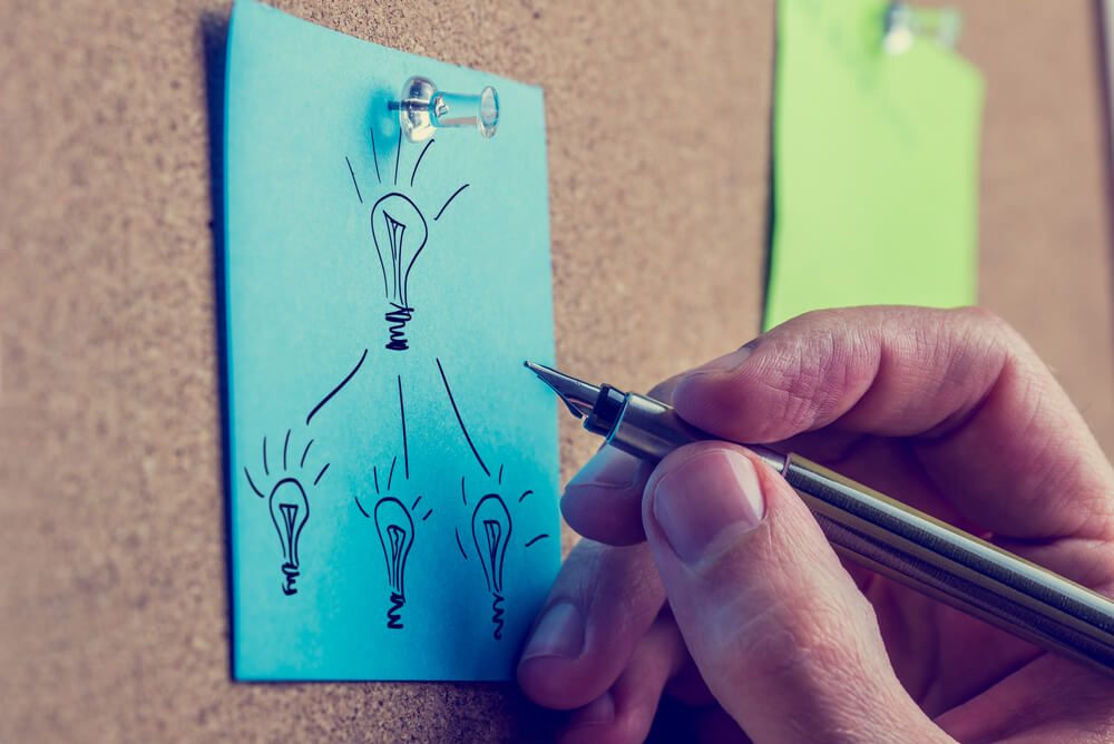 Retro image of the hand of a man working on a business plan writing on a blue sheet of paper on a notice board drawing a flow chart with light bulbs representing bright ideas.
